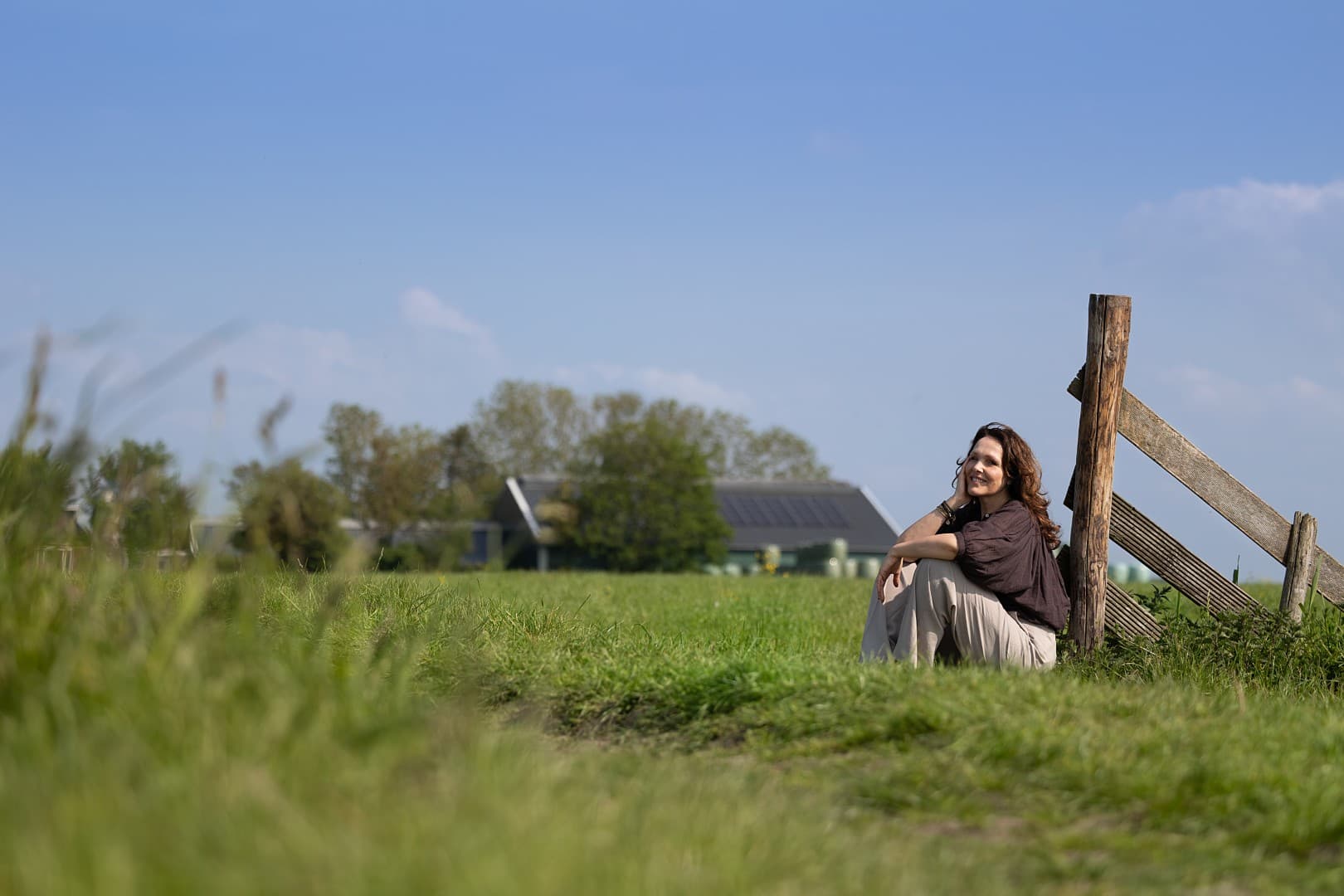 Albertha zittend in het gras bij een houten hek