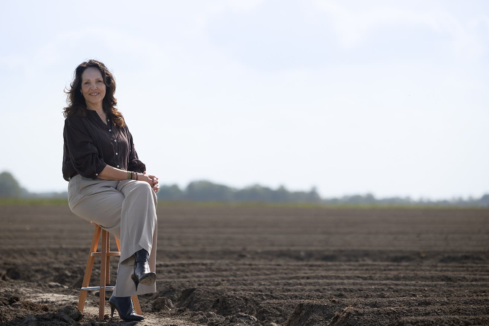 Albertha zittend op een kruk in een open landschap